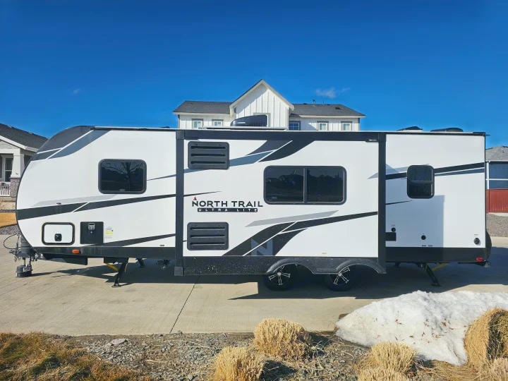 North Trail Ultra Lite travel trailer RV rental, parked on concrete in front of houses under a clear blue sky. Ready for adventure!. Heartland RVs North Trail 2024