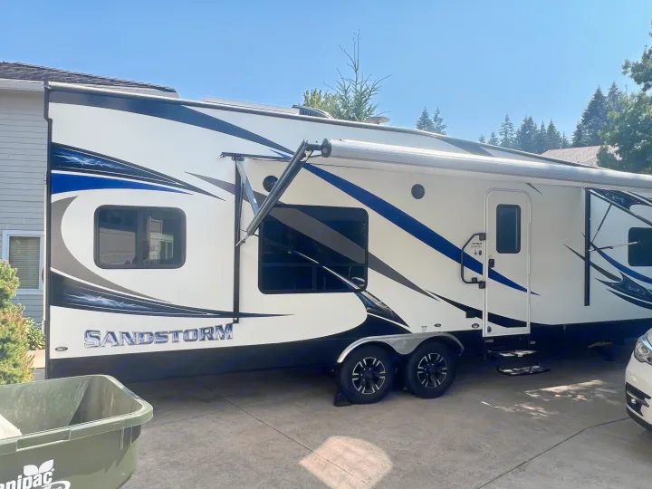 Spacious Sandstorm toy hauler RV rental, white with striking blue & black graphics, parked on a sunny driveway.. Forest River Sandstorm 2017