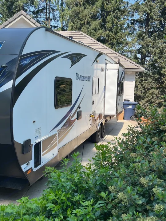 White Sandstorm RV rental parked on driveway, its slide-out extended. Ideal for camping and road trips.. Forest River Sandstorm 2017