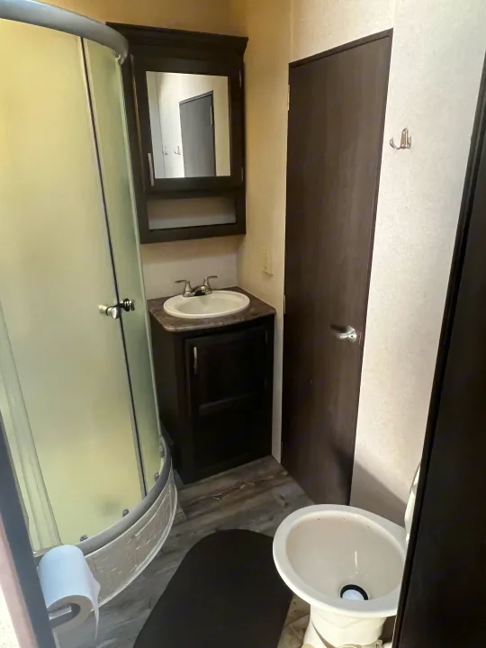 This RV rental bathroom features a curved glass shower, a sink vanity, toilet, and wall hooks for convenience.. Forest River Sandstorm 2017