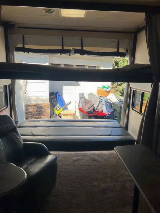 RV interior looking out open ramp door. Features bunk beds, chair, and a garage view with outdoor gear. Ideal RV rental.. Forest River Sandstorm 2017