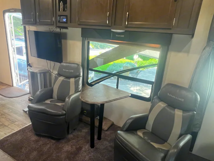 Spacious RV rental interior with two comfortable recliners, a table, and mounted TV, perfect for cozy travel adventures.. Forest River Sandstorm 2017