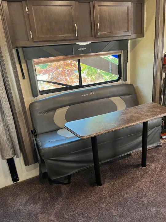 An RV rental's dinette area, featuring a long table, gray bench seating, and wood-like overhead cabinets.. Forest River Sandstorm 2017