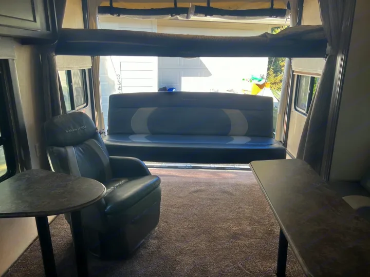 Spacious rv rental toy hauler interior: living area with recliner, sofa, and bunk, facing an open rear ramp.. Forest River Sandstorm 2017
