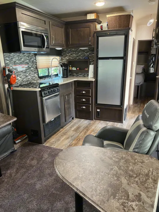 This RV rental features a well-equipped kitchen with dark cabinets, stainless appliances, and a comfy armchair, ideal for travel.. Forest River Sandstorm 2017