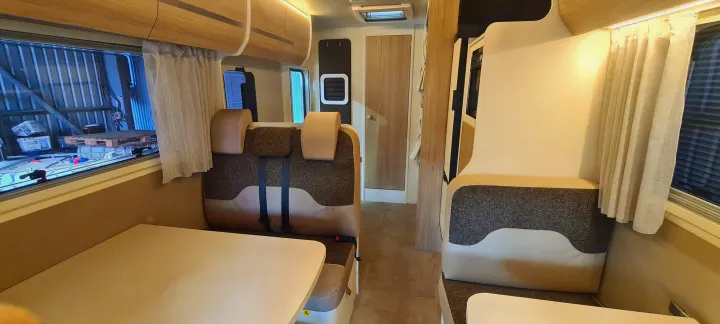 Spacious rv rental interior showing a comfortable dining area with upholstered seating, overhead storage, and windows.. Ford Transit Rimor Evo Sound 7 2022