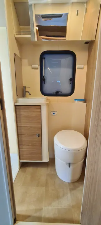 Compact RV rental bathroom featuring a sink, toilet, window, and efficient overhead storage, maximizing comfort on the go.. Ford Transit Rimor Evo Sound 7 2022