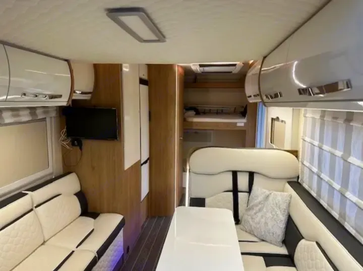 Modern rv rental interior: compact living area with white/black seating, TV, and bunk beds. Ideal for compact living.. Fiat Ducato Rollerteam Autoroller 707 2021