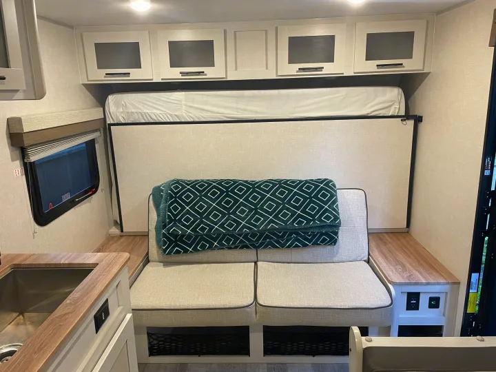Inside an RV rental: versatile living space with sofa seating, a pull-down bed, overhead cabinets, and a compact kitchen area.. No Boundaries NoBo 19.3 Essentials Only 2024