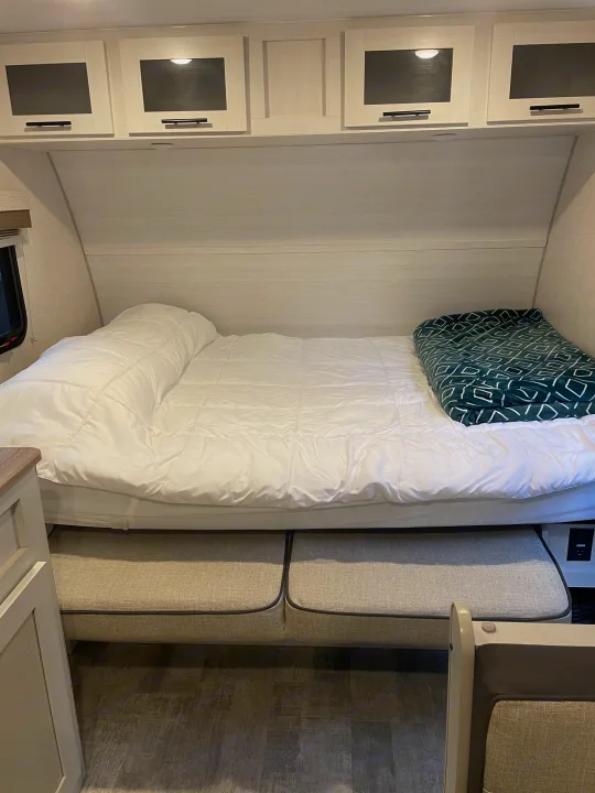 Comfortable RV rental bedroom with a cozy bed, overhead cabinets, and convertible dinette seating.. No Boundaries NoBo 19.3 Essentials Only 2024