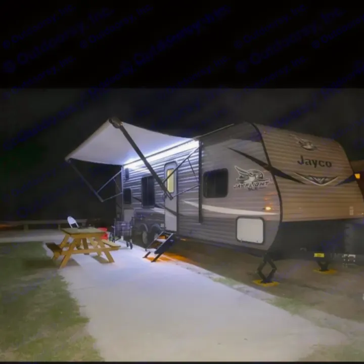 Night view of a Jayco RV rental at a campsite. Its bright awning lights illuminate the picnic table, ready for evening enjoyment.. Jayco Jay Flight SLX 2021