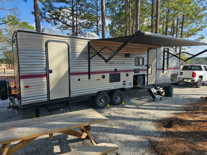 RV rental at a sunny campsite with an extended awning and picnic table, ready for outdoor adventure.. Forest River Cherokee Grey Wolf 2019