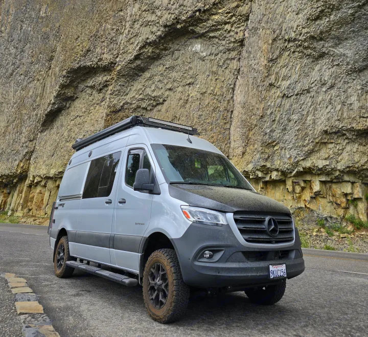 A gray Mercedes Sprinter rv rental, equipped for adventure, parked alongside a magnificent columnar basalt cliff.. Entegra Coach Launch 2023