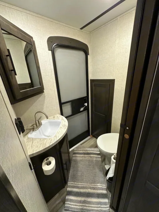 Compact RV rental bathroom featuring a sink, mirror, toilet, and a striped rug on the floor.. Crossroads RV Cruiser Aire 2022