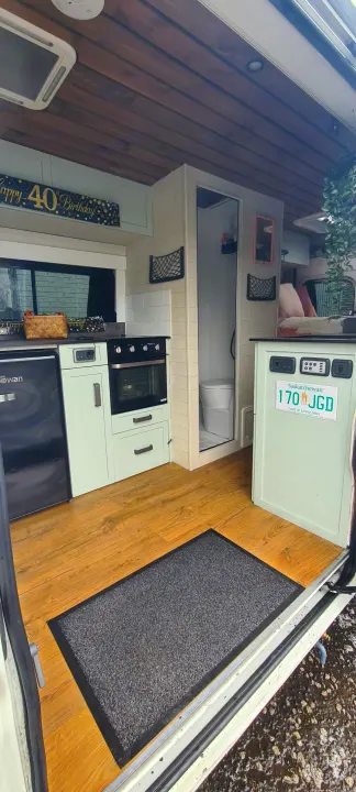 An RV rental's modern interior with light green kitchen cabinets, oven, fridge, and a compact bathroom. Adorned with a 'Happy 40th Birthday' banner.. Citroen Relay L3H2