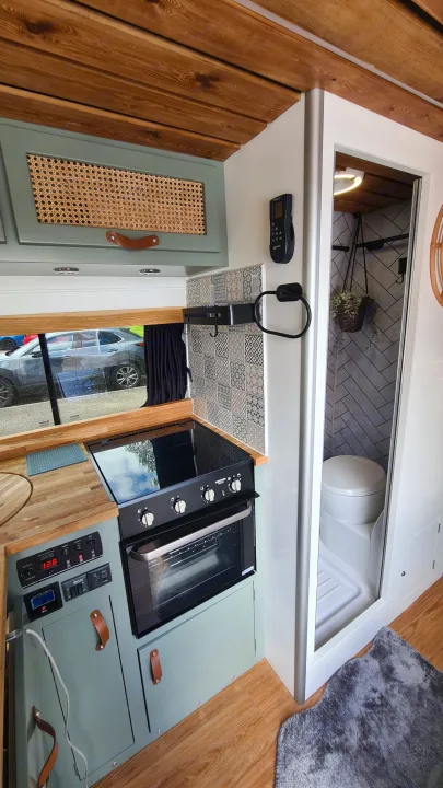 This RV rental interior offers a compact kitchen with an oven/stove, sage green cabinets, and a clever wet bath.. Citroen Relay L3H2 2022