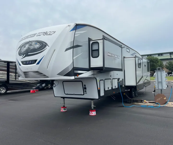 This Arctic Wolf fifth-wheel RV rental is parked with slide-outs extended and hooked up to utilities, ready for a camping trip.. Forest River Cherokee Arctic Wolf 2022