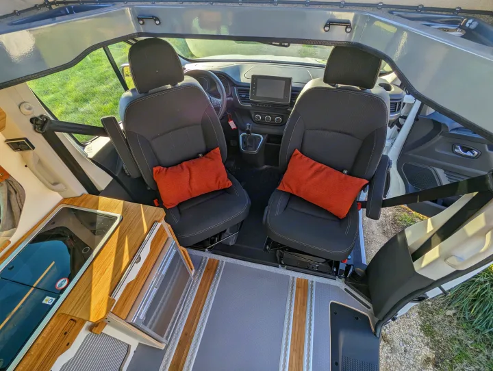 Explore this RV rental's cozy interior, featuring swivel front seats, a compact kitchen, and an open pop-top roof.. Renault Trafic 2025