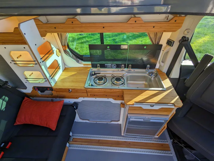 RV rental: Modern camper van interior. Features a compact kitchen with stove, sink, bamboo counters, modular storage, and a comfy seat.. Renault Trafic 2025
