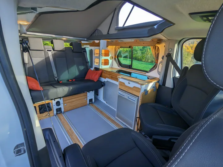 Interior of a modern camper van RV rental, featuring a pop-top, compact kitchen, and flexible seating for travel.. Renault Trafic 2025