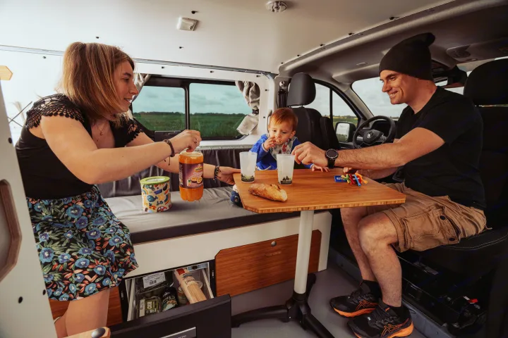 Family enjoying a moment in their RV rental, sharing snacks at the table. Perfect for memorable road trips.. Renault Trafic 2025