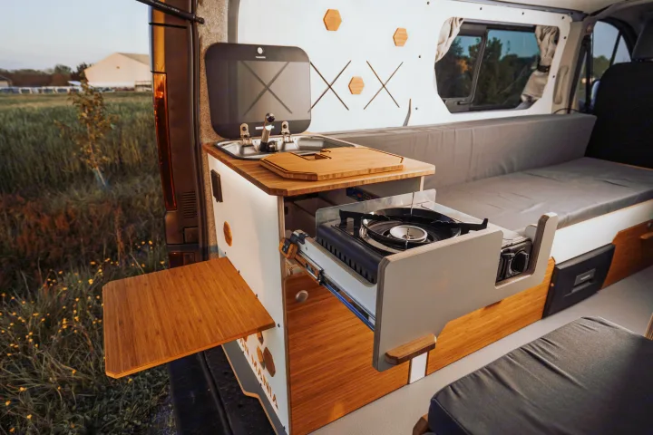 Modern RV rental interior: compact kitchen with sink, pull-out stove, bamboo counter, and comfortable bench/bed.. Renault Trafic 2025