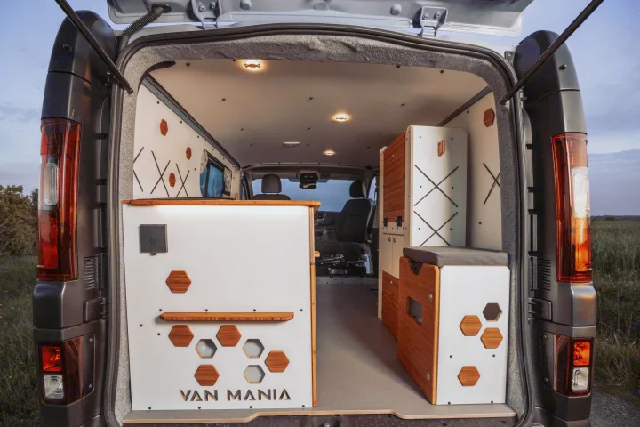 Modern rv rental camper van interior with rear doors open. Features stylish white and wood modular units, hex accents, and ceiling lights.. Renault Trafic 2025