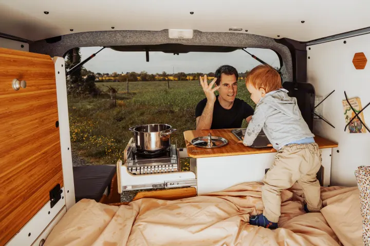 Cozy RV rental adventure: A dad and toddler interact in their camper van, complete with a functional kitchen and scenic view.. Renault Trafic 2025