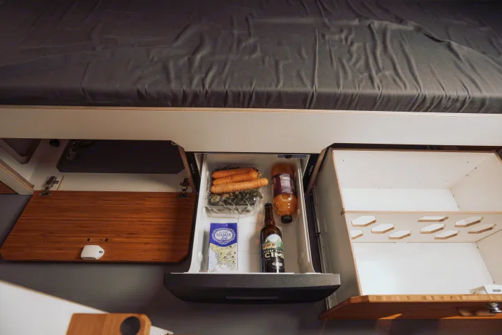 Compact RV rental interior: pull-out fridge with veggies & drinks, smart storage, and a comfy bed for road trips.. Renault Trafic 2025