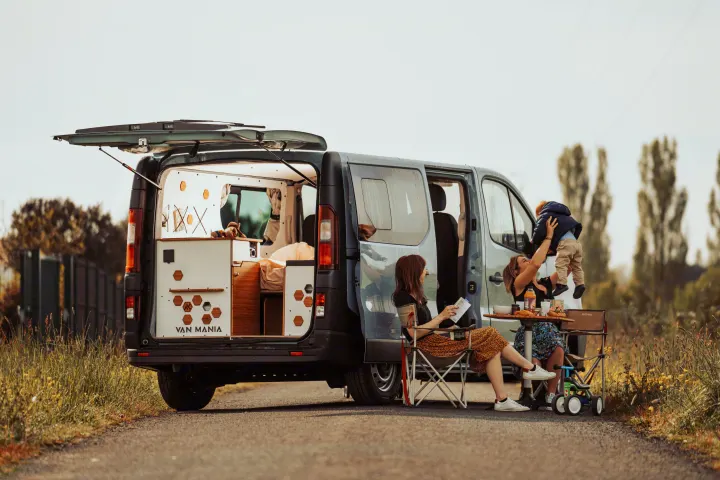 An RV rental from Van Mania showcases its custom interior, as a family enjoys an outdoor break with food and fun next to their camper van.. Renault Trafic 2025
