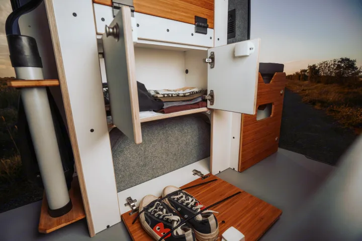 RV rental interior showcases smart storage with open cabinets, neatly folded clothes, and convenient shoe organization.. Renault Trafic 2025