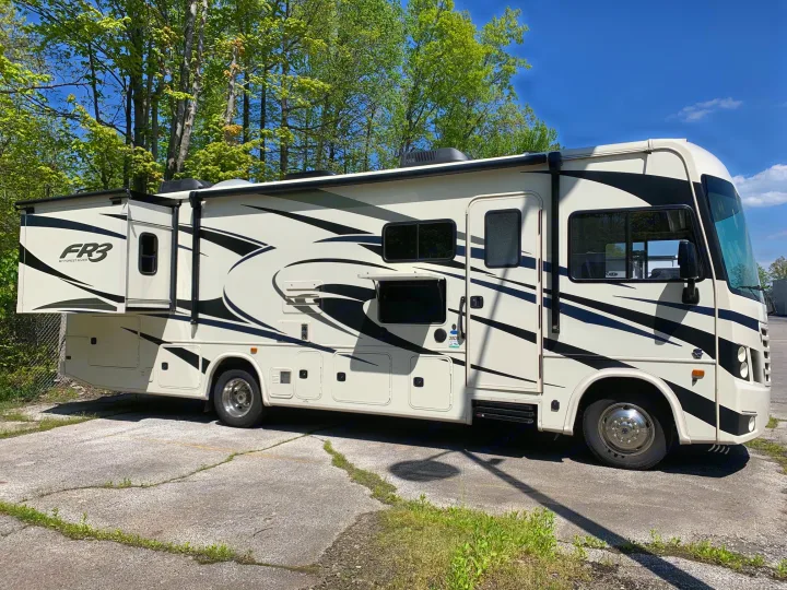 White and black motorhome rental, an FR3 RV with an extended slide, parked outdoors under a sunny sky.. Forest River Fr3 2021