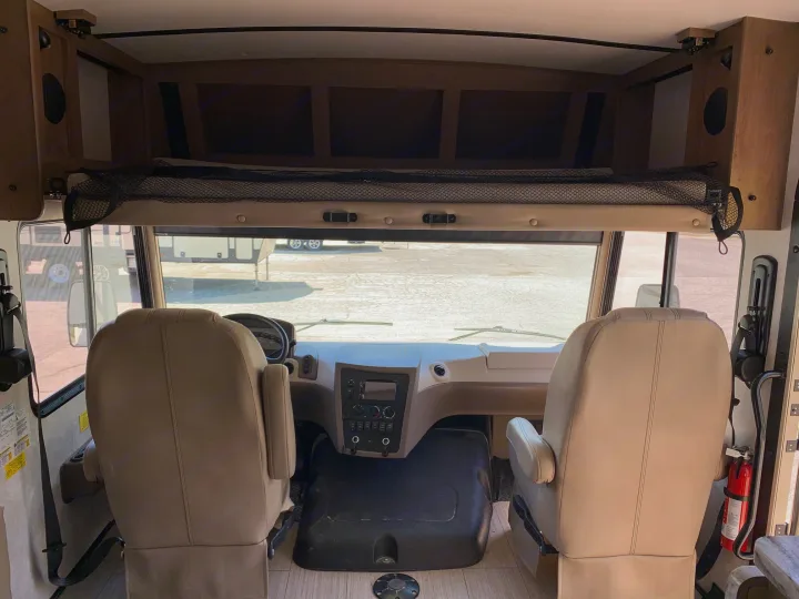 Inside an RV rental, showing the front cockpit with driver/passenger seats, dashboard, and overhead bunk/storage area.. Forest River Fr3 2021