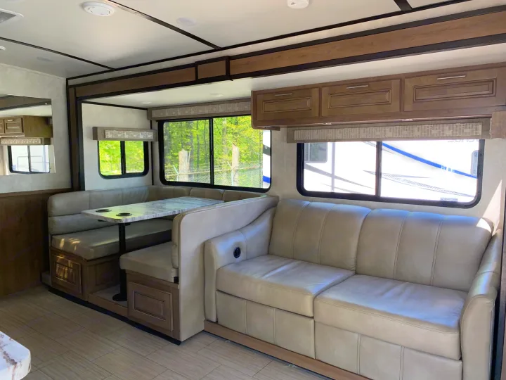View of a modern RV rental living space, featuring a tan sofa, dinette, and overhead cabinetry.. Forest River Fr3 2021