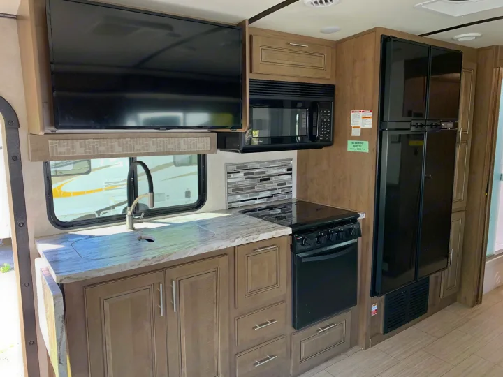 An RV rental's well-equipped kitchen featuring a TV, microwave, refrigerator, stove, sink, and cabinetry.. Forest River Fr3 2021