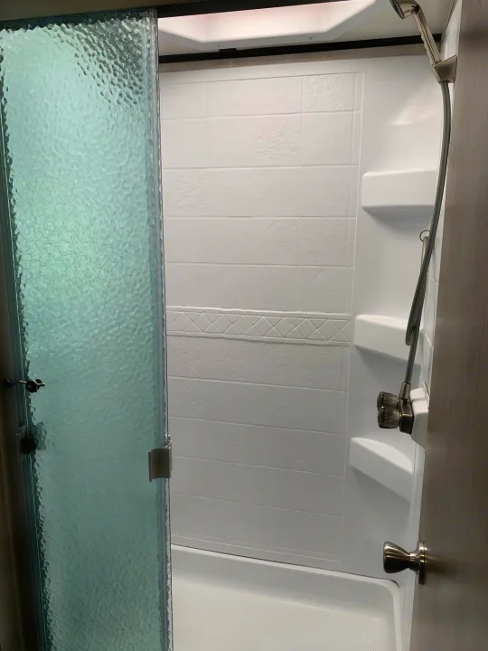 Clean and functional RV rental shower with a textured glass door, handheld showerhead, and built-in shelves.. Forest River Fr3 2021
