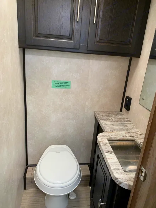 RV rental bathroom with toilet, vanity, and sink. A green sign above the toilet advises using only RV/marine toilet paper.. Forest River Fr3 2021