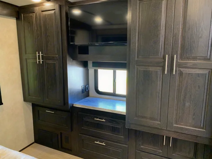 Explore this RV rental's well-equipped bedroom: dark wood cabinets, drawers, counter space, and a TV for your comfort.. Forest River Fr3 2021