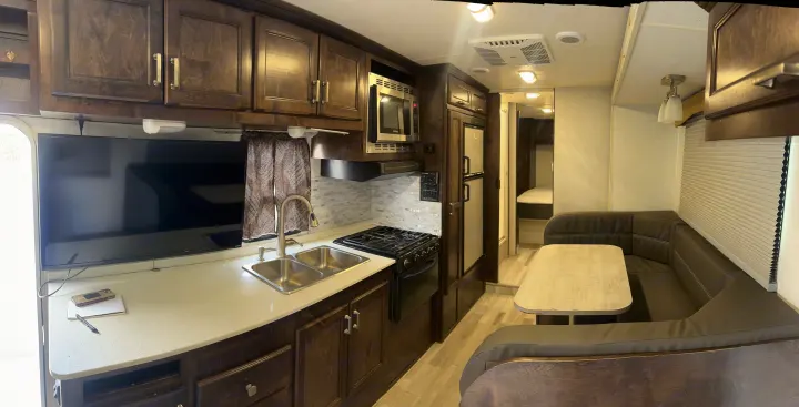 This RV rental interior features a modern kitchen with a TV, full amenities, a comfortable dining booth, and a hallway to the bedroom.. Winnebago Minnie Winnie 2015