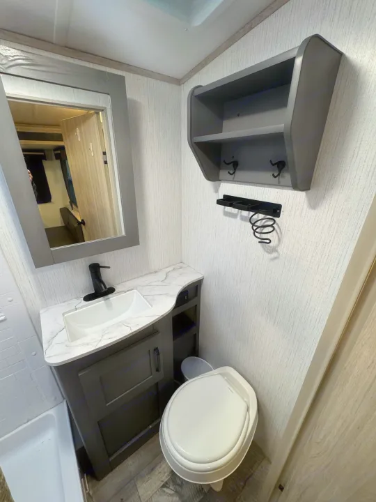 Compact RV rental bathroom with sink, mirror, toilet, and smart storage solutions. Ideal for travel comfort.. Heartland Sundance 2023