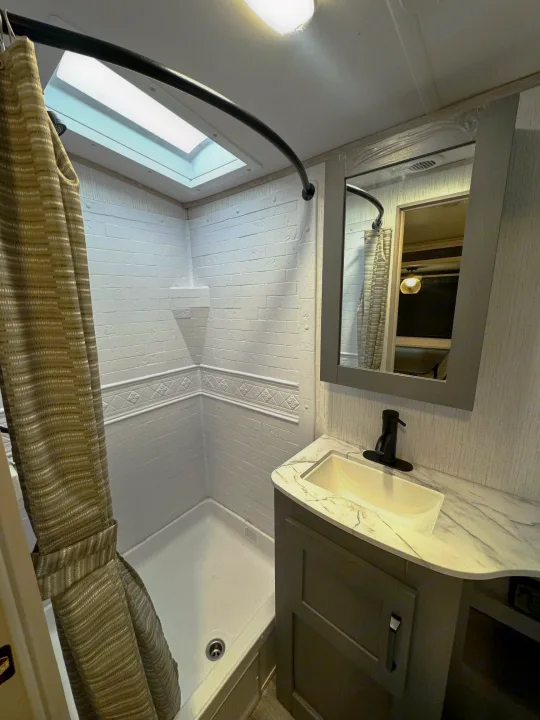 RV rental bathroom with a modern shower, skylight, and vanity. Ideal for comfortable travel and camping.. Heartland Sundance 2023