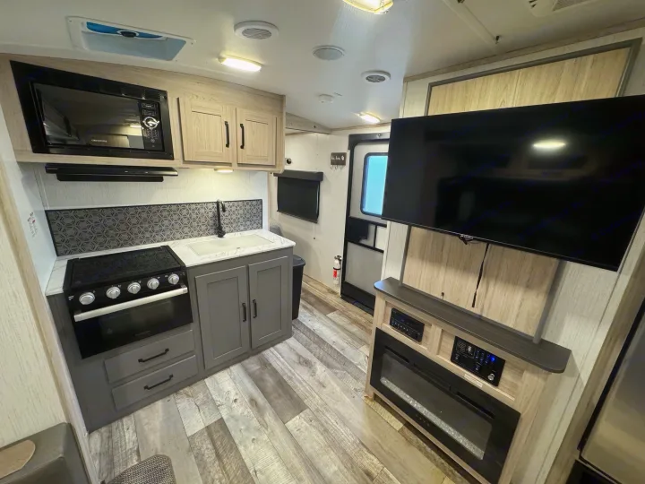 Spacious rv rental interior featuring a full kitchen with microwave, stove, sink, and cabinets, plus a TV & fireplace.. Heartland Sundance 2023