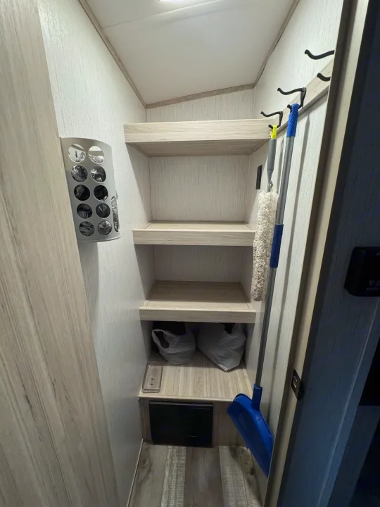 RV rental pantry: clever storage with shelves, broom, duster, and bag dispenser for compact living.. Heartland Sundance 2023