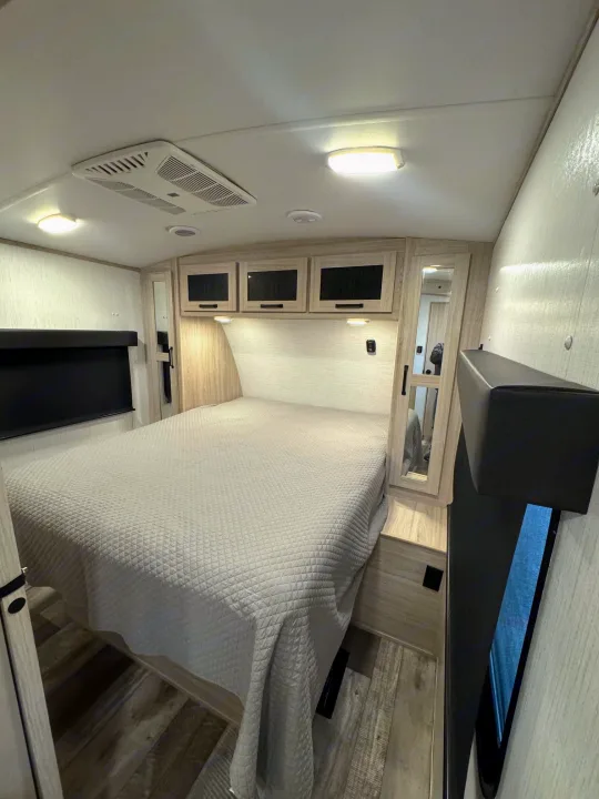 RV rental bedroom with queen bed, overhead storage, and AC unit. Compact and comfortable space.. Heartland Sundance 2023