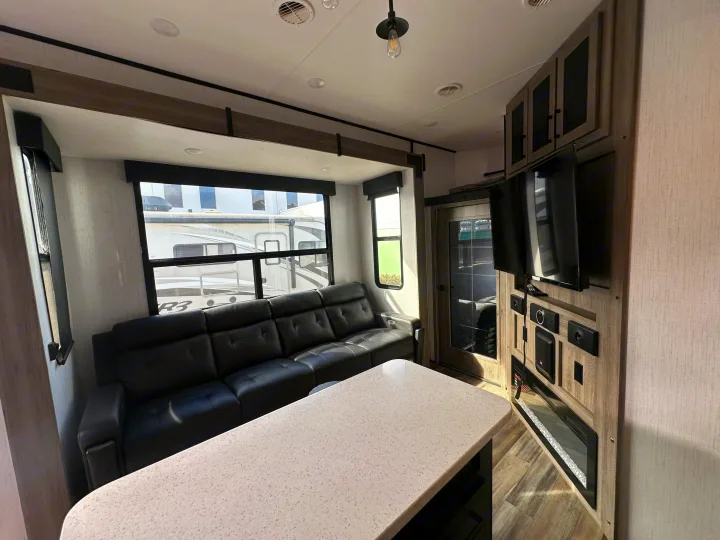 Cozy RV rental living area with black leather sofa, fireplace, island, and large windows offering exterior views.. Heartland RVs Road Warrior Toy Hauler 2022