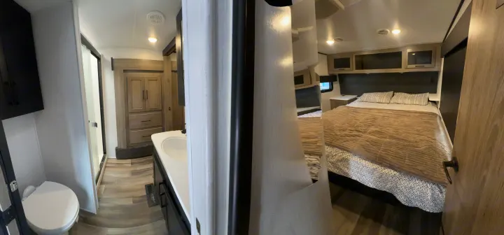 Inside this RV rental: A panoramic view showing a compact bathroom with toilet & sink, leading into a cozy bedroom with a bed.. Heartland RVs Road Warrior Toy Hauler 2022