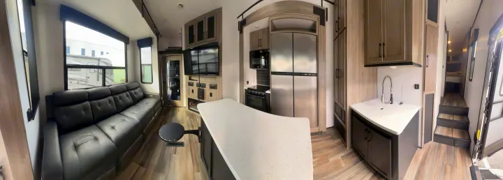 Modern RV rental: wide view of living area with sofa, kitchen with stainless appliances, and steps to sleeping space.. Heartland RVs Road Warrior Toy Hauler 2022