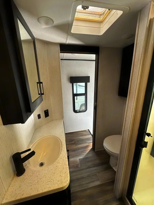 Inside an RV rental: a clean, modern bathroom with a sink, mirror, toilet, skylight, and wood-look flooring.. Heartland RVs Road Warrior Toy Hauler 2022
