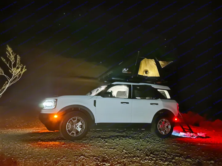 White SUV with roof-top tent set up for night camping. A great alternative to traditional rv rental for overland adventures.. Ford Bronco sport 2022