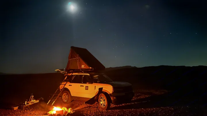 RV rental SUV with rooftop tent, ladder, & campfire under a starry, moonlit desert sky.. Ford Bronco sport 2022